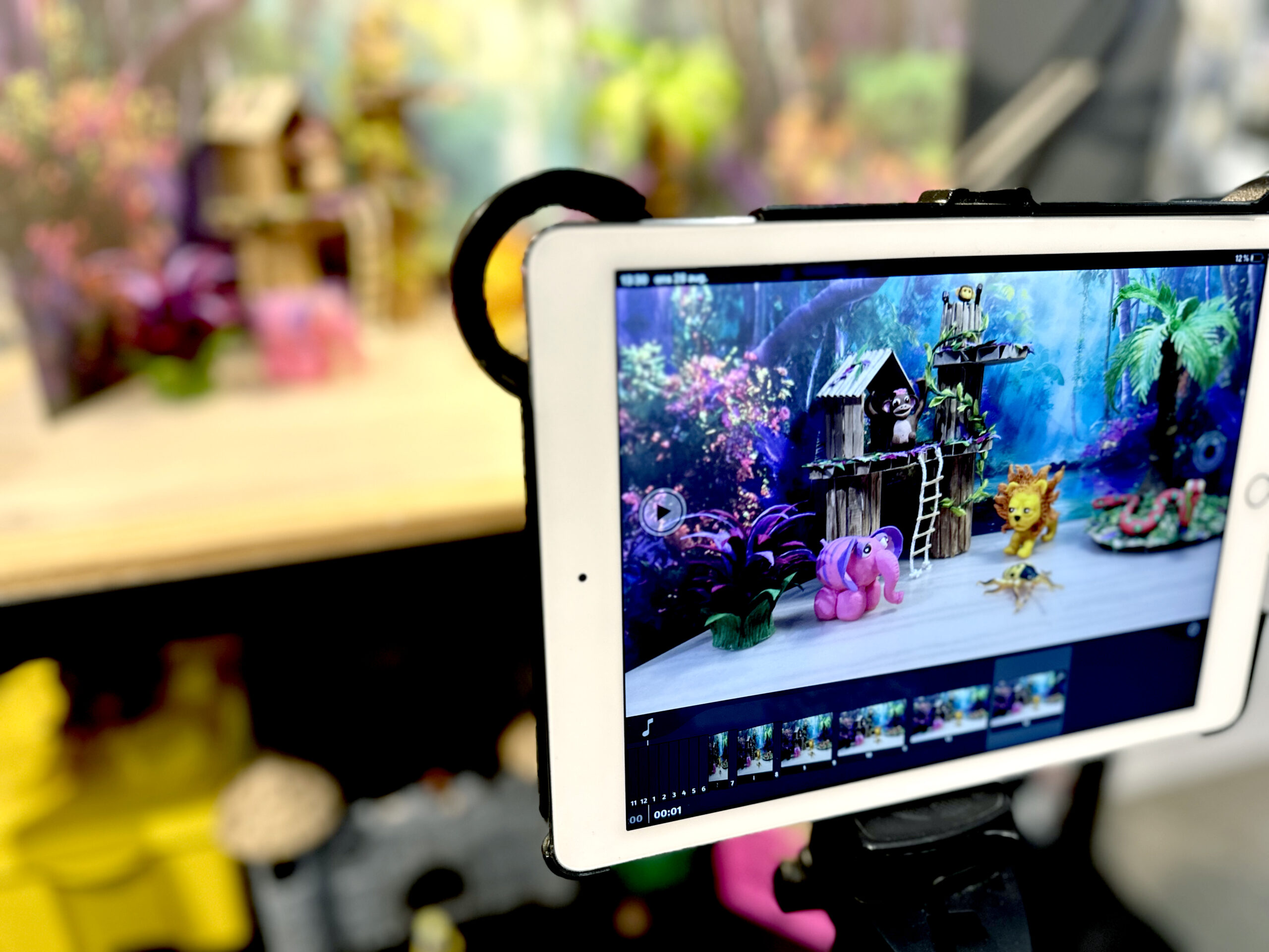 djungeln en ipad syns i förgrunden som står riktad mot en scen där färgglada figurer är utplacerade framför kameran i en djungelliknande miljö.